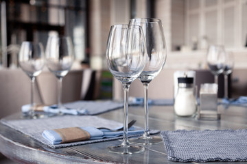 Restaurant interior, modern setting, wine and water glasses, forks and knives on textile napkins stand in row on vintage wooden table. Concept banquet, birthday, conference, group lunch