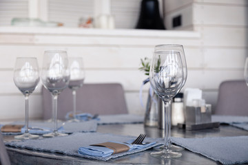 Restaurant interior, modern setting, wine and water glasses, forks and knives on textile napkins stand in row on vintage wooden table. Concept banquet, birthday, conference, group lunch