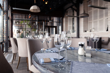 Restaurant interior, modern setting, wine and water glasses, forks and knives on textile napkins stand in row on vintage wooden table. Concept banquet, birthday, conference, group lunch