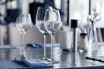 Restaurant interior, modern setting, wine and water glasses, forks and knives on textile napkins stand in row on vintage wooden table. Concept banquet, birthday, conference, group lunch