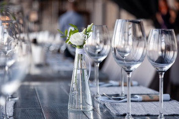 Modern restaurant setting, glass vase with bouquet flowers on table in restaurant. Wine and water glasses stand on wooden table. Concept banquet, birthday, conference, wedding