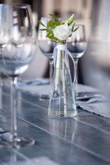 Modern restaurant setting, glass vase with bouquet flowers on table in restaurant. Wine and water glasses stand on wooden table. Concept banquet, birthday, conference, wedding