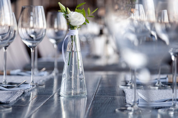 Modern restaurant setting, glass vase with bouquet flowers on table in restaurant. Wine and water glasses stand on wooden table. Concept banquet, birthday, conference, wedding