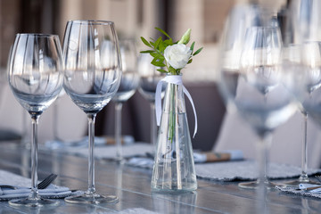 Modern restaurant setting, glass vase with bouquet flowers on table in restaurant. Wine and water glasses stand on wooden table. Concept banquet, birthday, conference, wedding