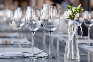 Modern restaurant setting, glass vase with bouquet flowers on table in restaurant. Wine and water glasses stand on wooden table. Concept banquet, birthday, conference, wedding