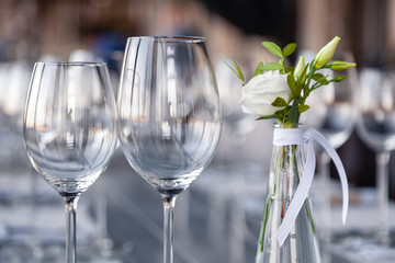 Modern restaurant setting, glass vase with bouquet flowers on table in restaurant. Wine and water glasses stand on wooden table. Concept banquet, birthday, conference, wedding