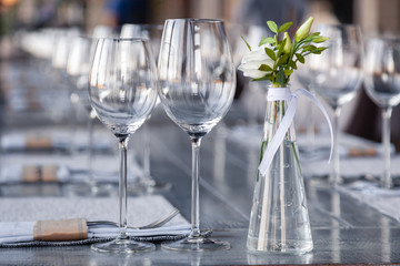 Modern restaurant setting, glass vase with bouquet flowers on table in restaurant. Wine and water glasses stand on wooden table. Concept banquet, birthday, conference, wedding
