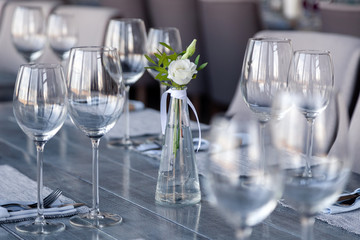 Modern restaurant setting, glass vase with bouquet flowers on table in restaurant. Wine and water glasses stand on wooden table. Concept banquet, birthday, conference, wedding