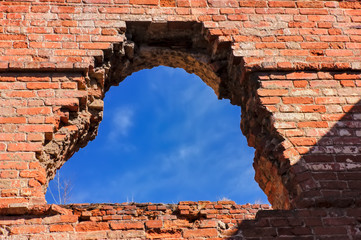 Destroyed window opening in an old red brick building against a blue sky.