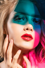Close-up face of a beautiful young blonde girl with red lips and her face is covered with colored shadows from multi colored pieces of transparent plastic. Fashion, commercial and conceptual