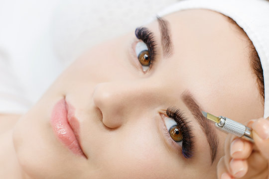 Beautiful young girl with long eyelashes tweezing her eyebrows in a beauty salon. Woman doing eyebrow permanent makeup correction . Microblading brow.