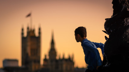 Child climbing a lamp post in South Bank in London (UK) at sunset with the Houses of Parliament in...