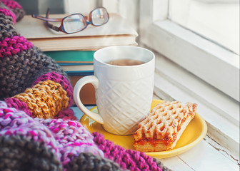 A сup of hot tea, stack of books and glasses on the background of a knitted blanket. 