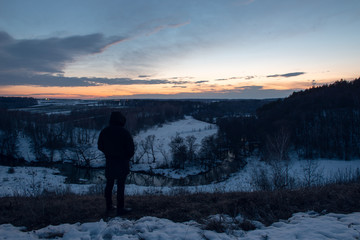Man stands on a hill against the background of the river and sunset