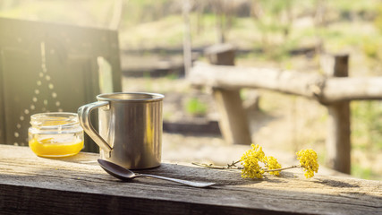 Metal mug, a jar of honey and flowering branch on a wooden table