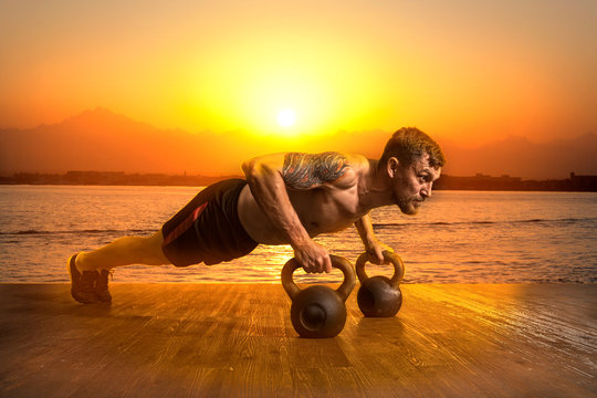 Muscular man doing pushups on kettleball