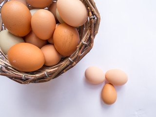Basket full of eggs on a white table with three eggs outside the basket. Top view. Landscape format.