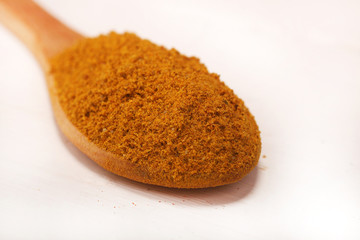 Wooden serving spoon full of curry spice powder isolated over the white background