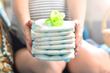 Stack of diapers and soother in the hands of a pregnant woman