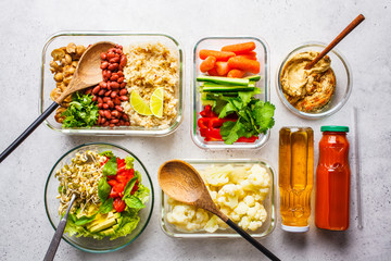 Healthy vegan food in glass containers, top view. Rice, beans, vegetables, hummus and juice.