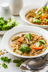 Lentil soup with vegetables in a white plate, white background, vertical. Plant based food, clean eating.