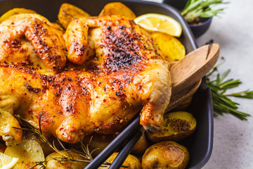 Fried whole tabaka chicken with potatoes in a grill pan, top view, white background.