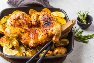 Fried whole tabaka chicken with potatoes in a grill pan, top view, white background.