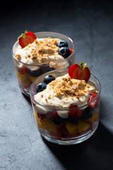fresh fruit with custard in glasses on a dark background, vertical