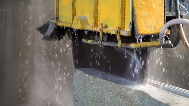 A cutting machine prepares slabs of marble and granite. Water and marble debris fly out in slow motion.