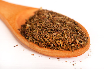 Wooden serving spoon full of dried basil spice isolated over the white background