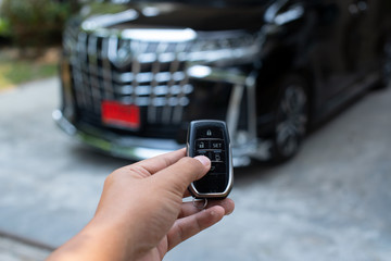 Men's hand holding car key ready to start a new car with blurred black car background.hand hold key blur car parking.