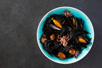 Top view of mediterranean black pasta with seafood. Spaghetti Nera with cuttlefish ink, mussels, shrimp and red chili pepper on blue plate. on dark background.
