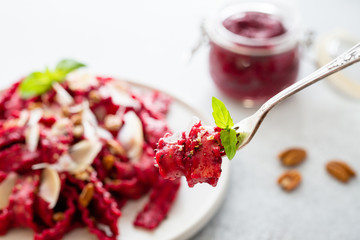 Close-up of fork with vegetarian mafaldine pasta with beet pesto sauce, walnut and parmesan cheese on a white background