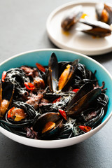 Mediterranean black pasta with seafood. Spaghetti Nera with cuttlefish ink, mussels, shrimp and red chili pepper on blue plate. on dark background.