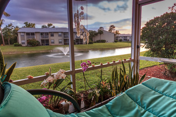 Swinging lounge chair on a lanai at sunset as it overlooks a pond with a fountain