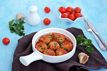 Fish meatballs in tomato sauce in a white ceramic pan on a light blue concrete background.