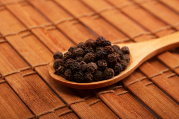 Wooden serving spoon full of black pepper spice over the wooden background