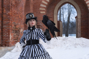 an elderly woman in a gothic dress with a black raven hat on nature in winter.