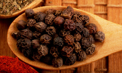 Wooden serving spoon full of black pepper spice over the wooden background