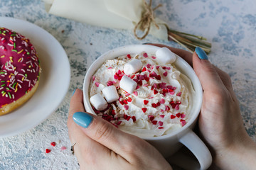 A cup of coffee with whipped cream and a berry pink donut