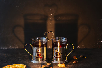 Two cups of fruit tea and a shape in the form of a heart, with a shadow on the wall. Concept for the day of lovers on a dark background