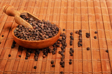 Wooden serving spoon shovel full of black pepper spice balls in wooden bowl isolated over the wooden background