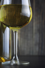 Transparent bottle of white dry wine on the table. White wine glass on a wooden background.