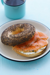 Poppy seeds bagel with cream cheese and smoked salmon served on a white plate with black rim. Blue table, high resolution