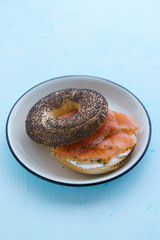 Poppy seeds bagel with cream cheese and smoked salmon served on a white plate with black rim. Blue table, high resolution