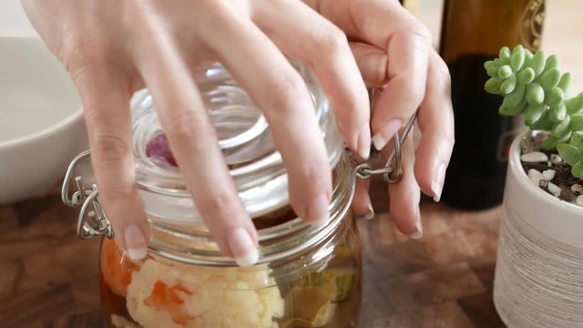 Jar of pickled vegetables is opened and spooned into a jar. 