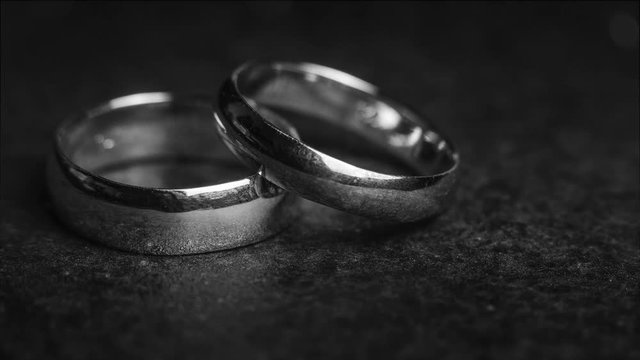 A pair of wedding ring bands on a dark stone background with floating bokeh and a zoom effect