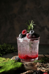 Refreshing summer drink with syrup, raspberry, blackberry and ice on dark background, Glass with cold and healthy beverage