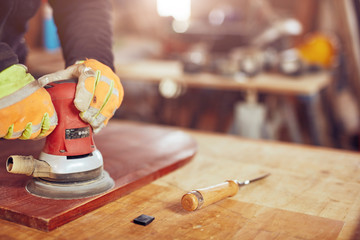 Male carpenter using orbital electric sander in a retro vintage workshop.