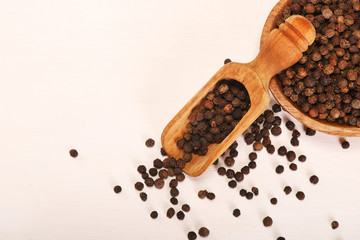 Wooden serving spoon shovel full of black pepper spice balls in wooden bowl isolated over the white background. Copy space